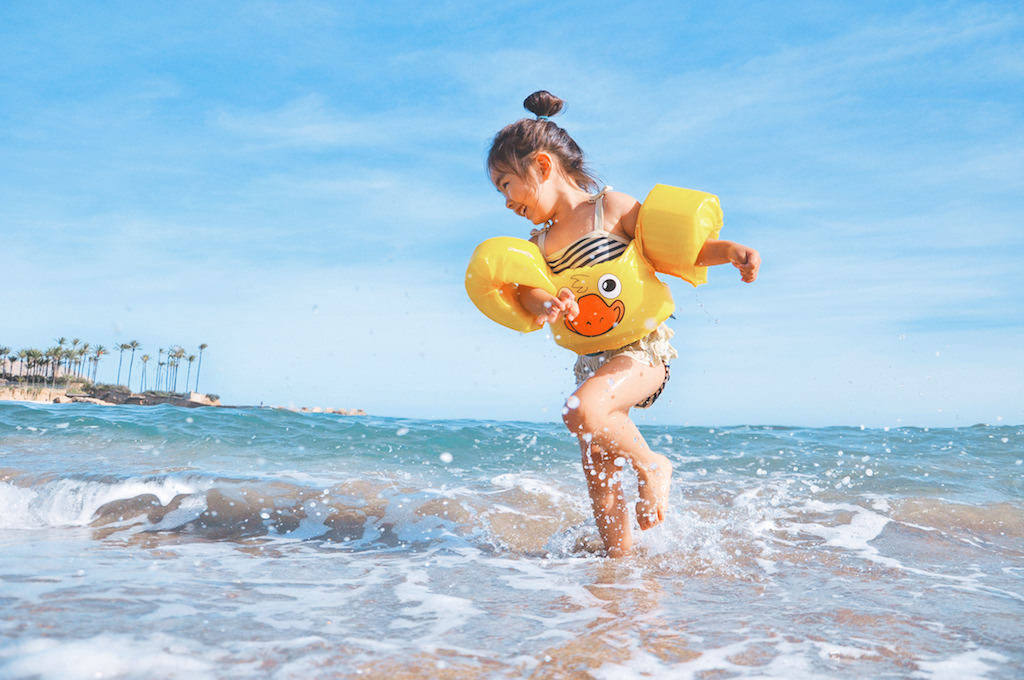 Girl in duck floaties playing in the beach water.